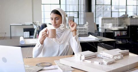 Female architect in modern design studio with laptop and scale model