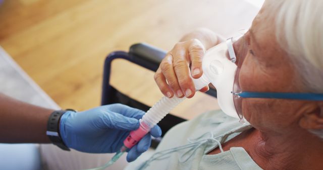 Elderly woman is receiving oxygen therapy from a caretaker, who is wearing gloves while adjusting the oxygen mask. This image can be used to illustrate healthcare, senior care, and medical assistance themes. Ideal for articles, presentations, and advertising materials focused on respiratory treatment, elderly care, nursing services, and medical support.