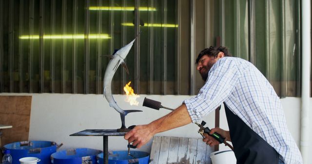 Male artist welding metal sculpture of a dolphin in a workshop. Great for illustrating themes of craftsmanship, dedication, metalworking, and creative arts. Suitable for use in articles about welding, artist profiles, DIY projects, creative studios, and handmade crafts.