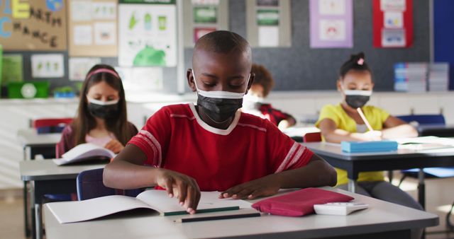 African american boy wearing face mask while studying in the class at school. hygiene and social distancing at school during covid 19 pandemic.