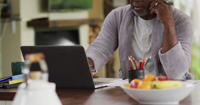 Senior Man Working from Home on Laptop with Stationery and Fruit Bowl - Download Free Stock Images Pikwizard.com