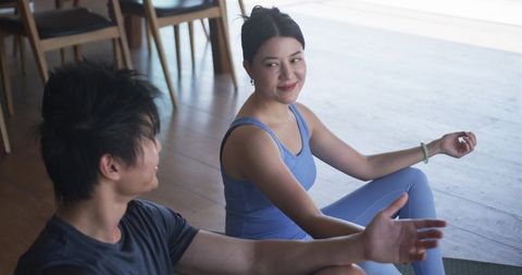 Young woman smiling and chatting after yoga with companion in bright home studio