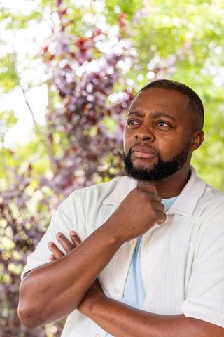 Contemplative african american man standing in garden holding chin with crossed arms