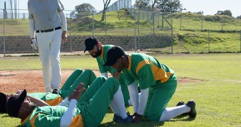 Baseball teammates tending injured player while kneeling on infield during sunny practice