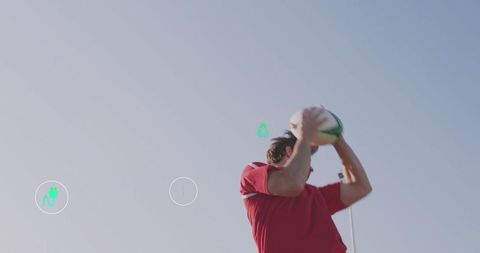 Athlete raising and throwing rugby ball into blue sky wearing red jersey sports action