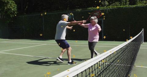 Seniors exchanging rackets at net on sunny tennis court celebrating active aging