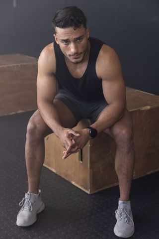 Muscular athlete sitting on plyometric box catching breath after intense gym workout rest