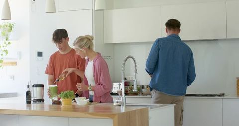 Family preparing pesto together in bright modern kitchen with wood island and blender