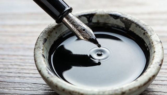 Fountain pen nib dropping ink droplet creating ripples in ceramic inkwell