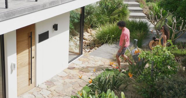 Couple walking towards entrance of a modern home surrounded by a lush, well-maintained garden. This can be used for promoting real estate, landscaping services, home improvement, lifestyle blogs, or summer activities.