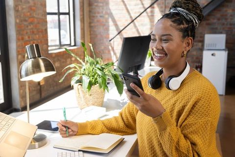 Smiling Woman Working at Desk in Loft Office with Smartphone