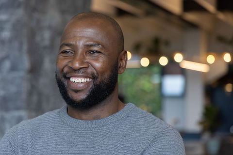 Confident african american man smiling in modern coworking lounge wearing gray sweater