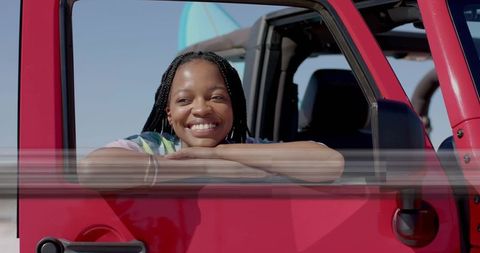 Smiling Adventurer Leaning on Red SUV at Sunny Beachside