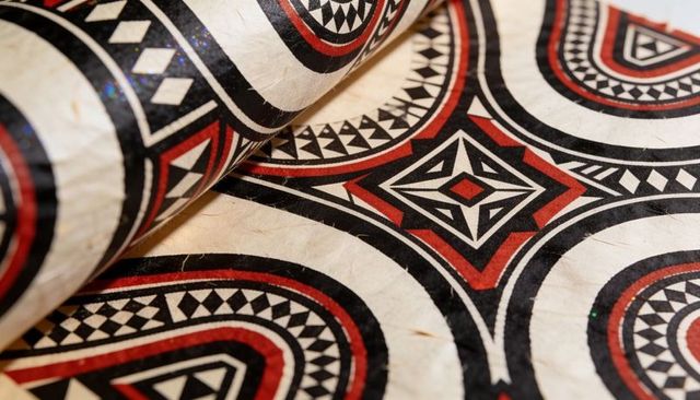 Curling handcrafted bark cloth displaying bold black and red geometric tribal pattern