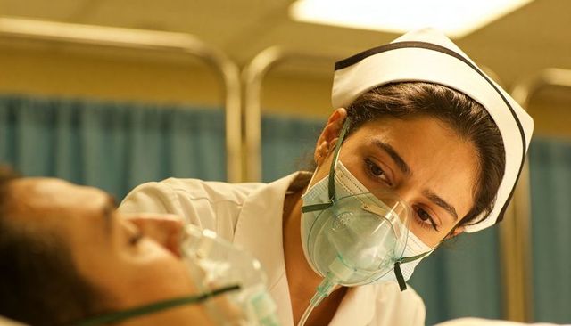 Compassionate nurse wearing protective mask giving oxygen therapy to patient in ward cubicle
