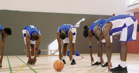 Basketball team stretching on indoor hardwood court before practice