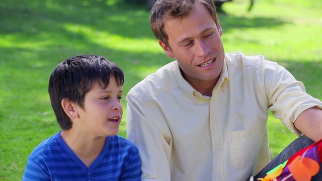 Father and son are enjoying quality time in the countryside while holding a colorful kite. The sun is shining, making it an ideal day for leisure activities. This video is suitable for themes related to family bonding, outdoor activities, parenting, and spending time together in nature. It can be used in advertisements, blogs, or articles focusing on family values and healthy lifestyles.