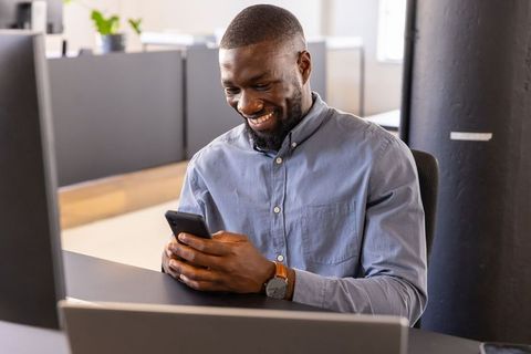 Professional Man Smiling While Checking Smartphone at Office
