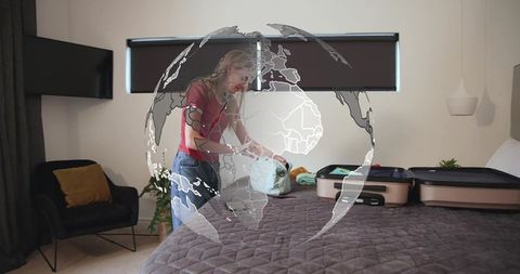 Packing carry-on for international trip: woman organizing luggage in bedroom with globe