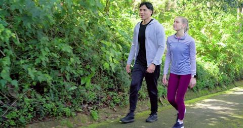 Young couple walking on sunlit woodland trail wearing activewear and smartwatch