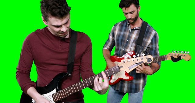 Two men are playing electric guitars, standing against a green screen background. One man wears a plaid shirt while the other wears a red shirt. This image is ideal for music-related themes, online tutorials, or green screen video projects allowing for various backdrop customization.