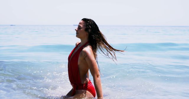 Depicts woman relaxing in ocean while wearing red swimsuit. Ideal for advertising summer vacations, beachwear, relaxation, lifestyle activities, travel brochures, or wellness products. Perfect for promoting beach destinations, fitness, and outdoor leisure.