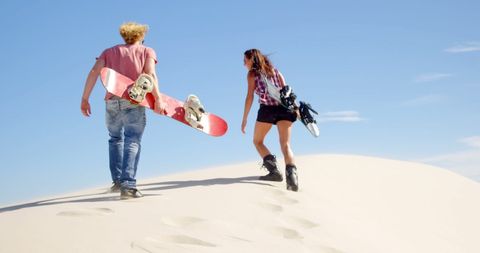 Adventurous couple hiking with snowboards on sand dune