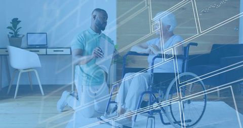 Male caregiver kneeling explaining digital care with tablet to elderly woman in wheelchair