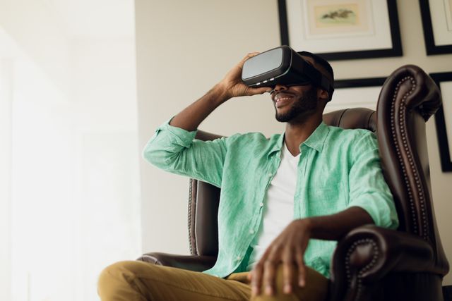 Side view  of an African-American sitting on a leather chair inside a room while wearing virtual goggles