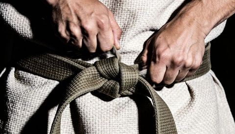 Martial artist tying khaki belt on textured gi preparing for training