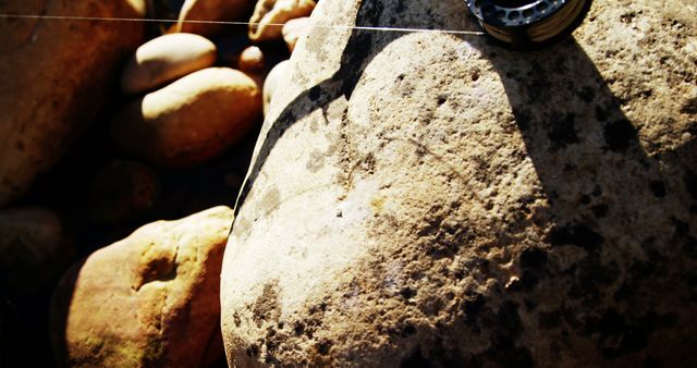 Close-up of large rocks with a fishing reel casting a shadow in natural light on a sunny day. Ideal for themes like fishing, outdoor activities, nature, and leisure. Suitable for use in blogs, articles, advertisements, and nature-focused projects.