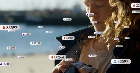 Blond woman holding compact camera by waterfront with floating social media notifications