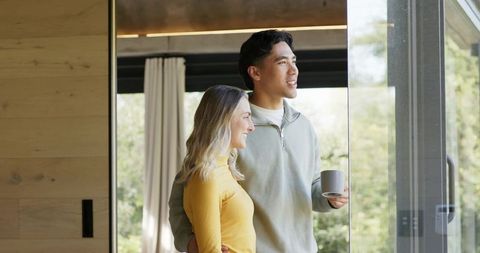Couple enjoying morning together by sliding glass door, holding coffee, garden view