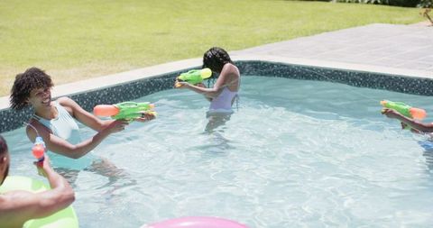 Family having fun with water pistols in outdoor pool together