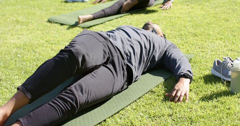 Partners lying on yoga mats in sunny park with shoes and water bottle nearby