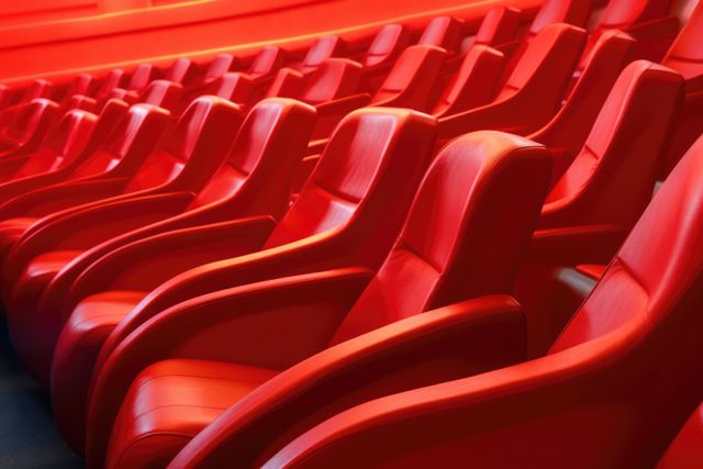 Rows of empty red seats create a vibrant pattern in a theater. The image captures the anticipation before an event or performance begins.