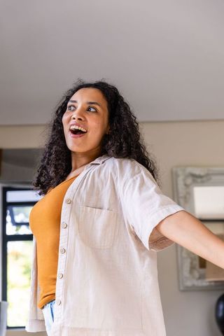 Joyful african woman speaking and gesturing in sunlit lounge wearing mustard tank and beige shirt