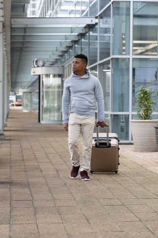 African american traveler walking with suitcase along modern glass transit terminal