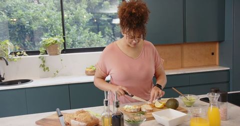 Preparing avocado toast at sunlit teal kitchen island with rustic bread and citrus