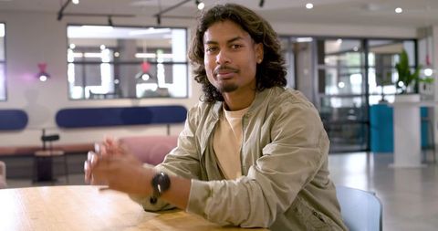 African american man sitting in modern coworking lounge wearing olive jacket and wristwatch