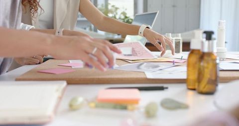 Creative team arranging sketches and sticky notes on corkboard during branding workshop