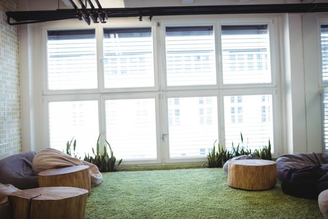This image depicts a modern office waiting room featuring natural elements such as indoor plants and wooden furniture. The green carpet adds a touch of nature, creating a relaxing atmosphere. Ideal for use in articles or advertisements related to office design, interior decor, or workplace wellness.