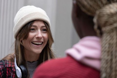 Young woman smiling and chatting with friend in hallway wearing beanie and headphones