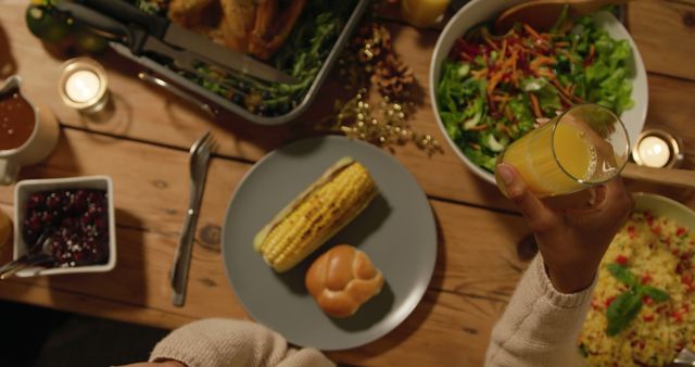 Top view of a dinner table featuring an array of healthy food options, including a corn on the cob, salad, and a refreshing glass of juice in someone's hand. Ideal for representing family gatherings, healthy eating, or festive meal settings.