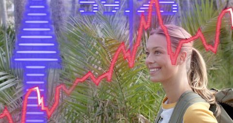 Smiling woman hiking among palms with augmented analytics overlays and backpack