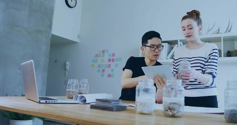 Startup team collaborating in modern studio reviewing tablet and inspecting glass jars of seeds