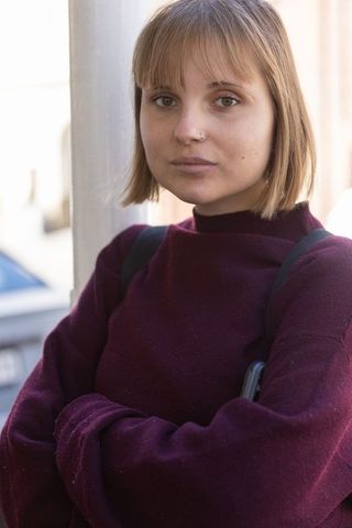 Urban portrait of young woman with nose stud, arms crossed, burgundy sweater