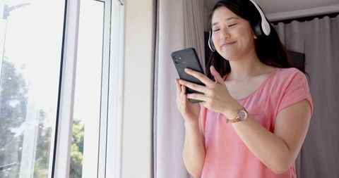 Asian Woman Enjoying Music on Smartphone with Wireless Headphones at Home