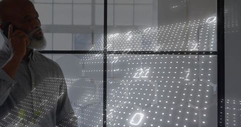 Senior executive talking on smartphone by digital binary overlay in modern glass office