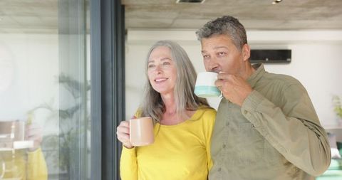 Senior Couple Enjoying Morning Coffee by Glass Door at Home